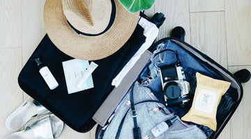 Open suitcase with clothes, straw sun hat and camera